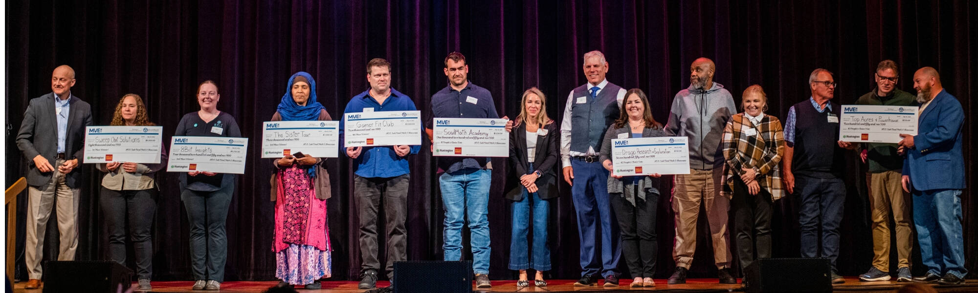 MVE Lab Final Pitch Traverse City - Men and women standing on stage holding big paper checks
